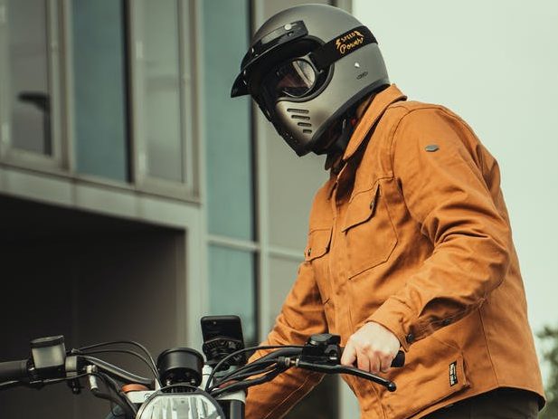 portrait of man in orange jacket holding motorcycle