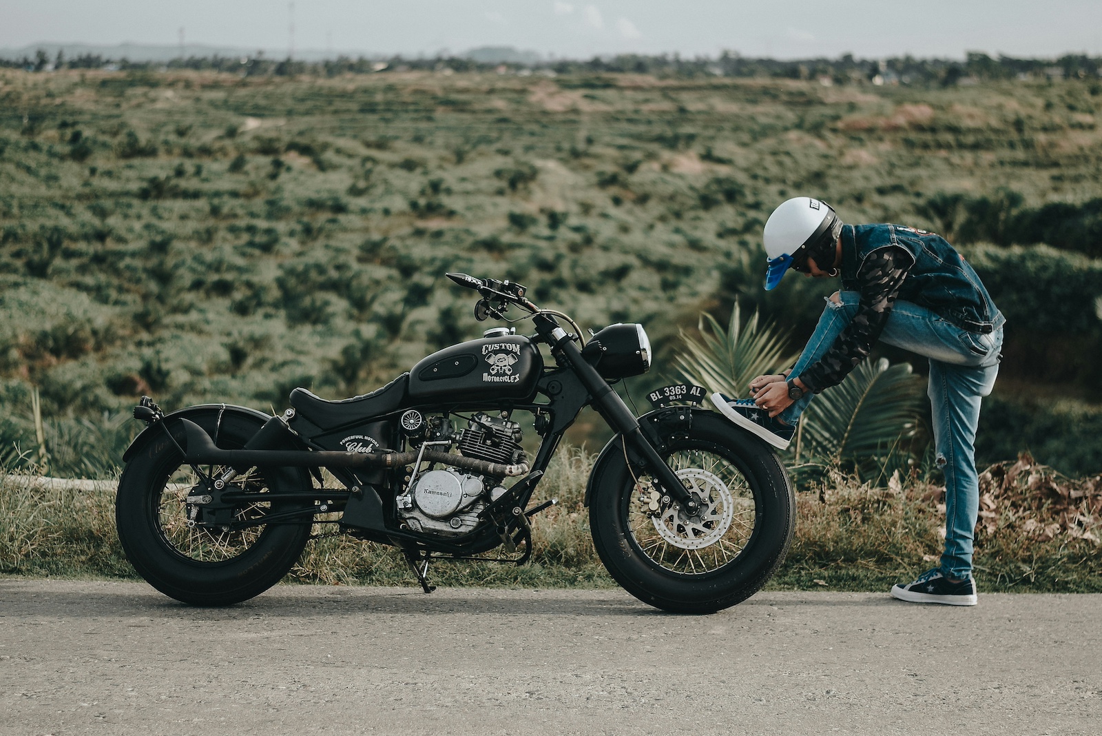 A motorcycle rider standing with his parked bike while wearing a half helmet.