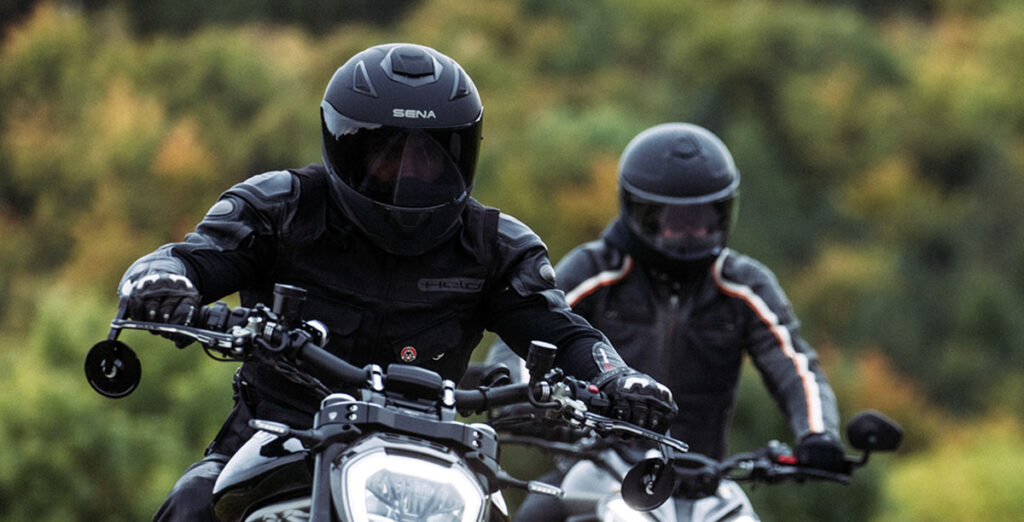 Two motorcycle riders wearing Sena motorcycle helmets with Bluetooth intercoms.
