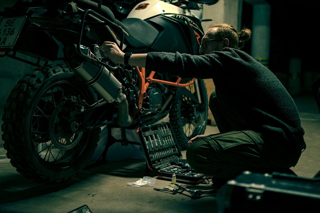 A man performing maintenance on his motorcycle inside his garage. 