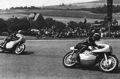 Phil Read leads a 4-stroke Honda on the 2-stroke Yamaha at the 1964 East Germany Grand Prix at the Sachsenring
