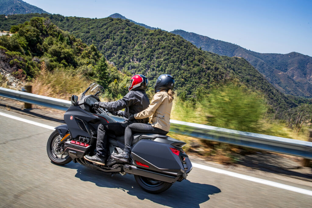 A black Honda Gold Wing with two riders riding on a canyon road. 