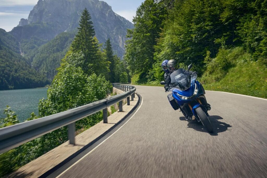 2025 Honda NT1100 DCT riding on a mountain road next to a lake.