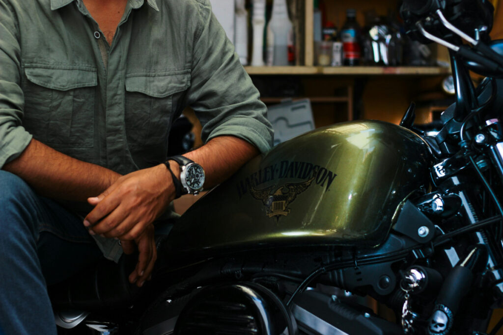 A motorcyclist sitting with his Harley-Davidson wearing a watch.